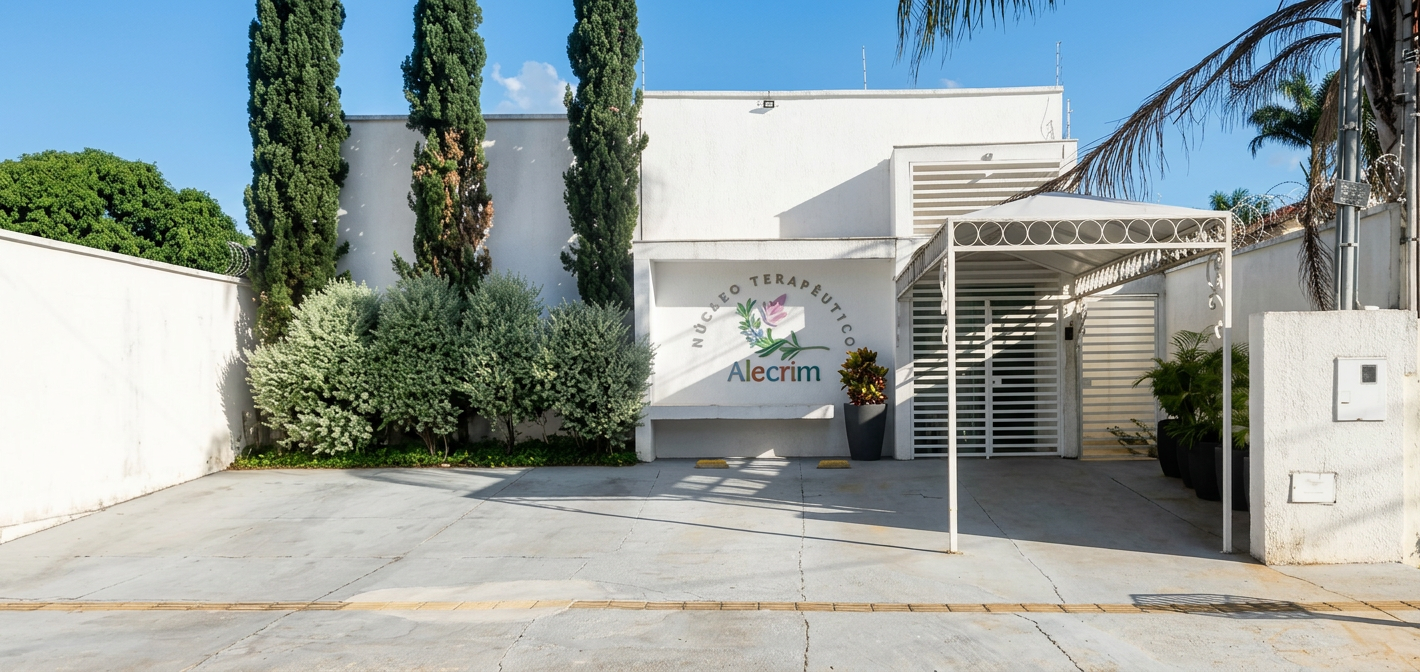 Fachada branca do Núcleo Terapêutico Alecrim em Goiânia, com logo na parede e entrada coberta